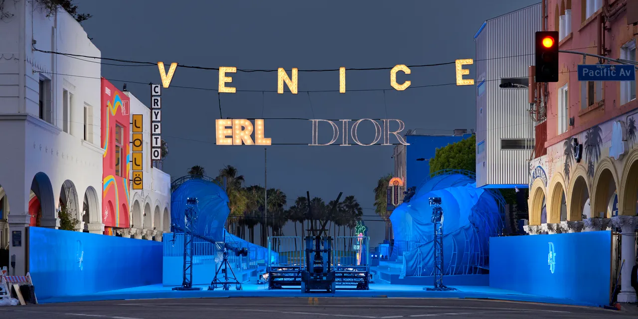 DIOR HOMME — VENICE and ERL DIOR lit over the street after dark, the set ready